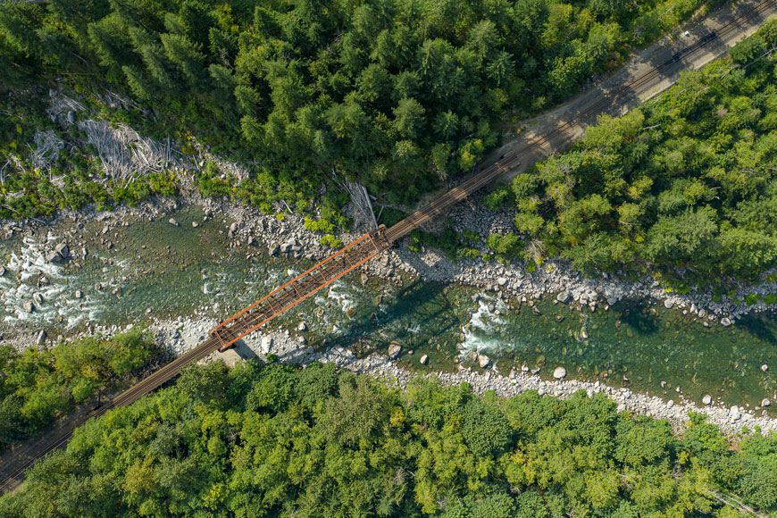 A narrow channel of water flows under a train bridge in the Pacific Northwest