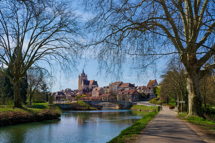 A canal stretches beside a park path and winds under a scenic bridge in an old European town