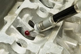 A CMM probe topped with a red bead measures an aluminum casting