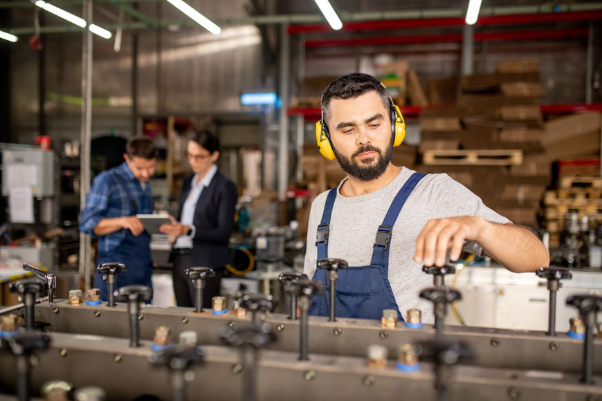 A young factory worker wearing ear protection works on an industrial machine