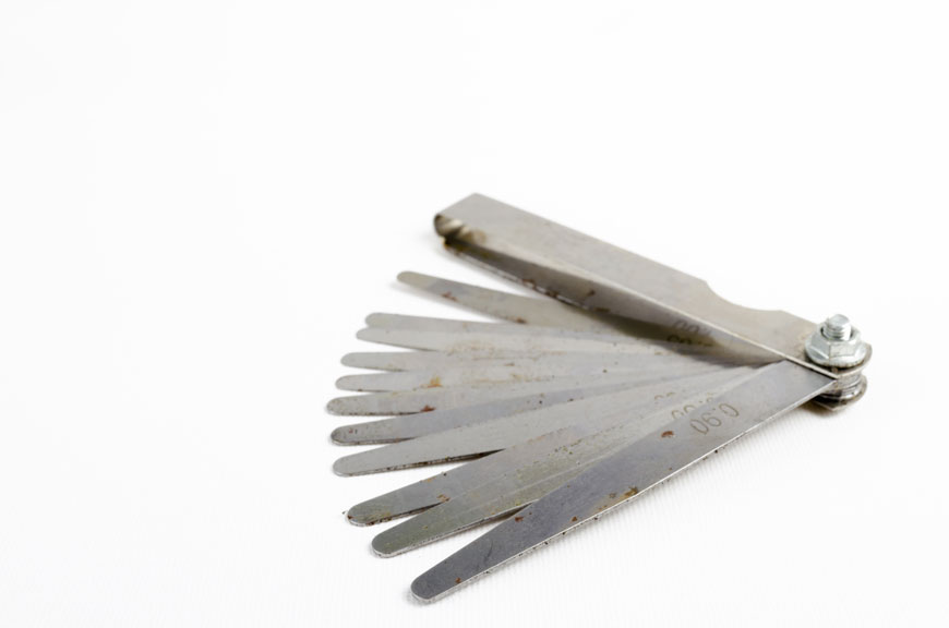 A studio photograph of a set of used feeler gauges showing some light rust