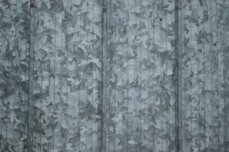 A sheet of galvanized steel is covered in large leaf-like spangles of dark grey, light grey, and silver