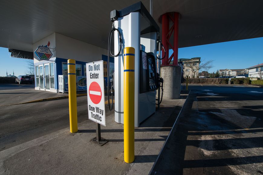 Yellow safety bollards with blue reflective tape protect a gas pump at a gas station