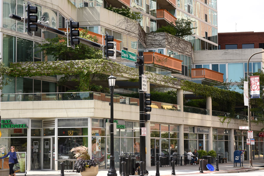 An ivy colored building is ringed with attractive bollards, planters, and lamp standards