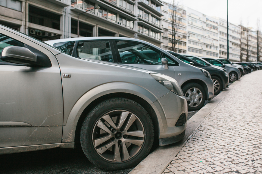 A line of cars are nose-in angle parked over a curb in Portugal