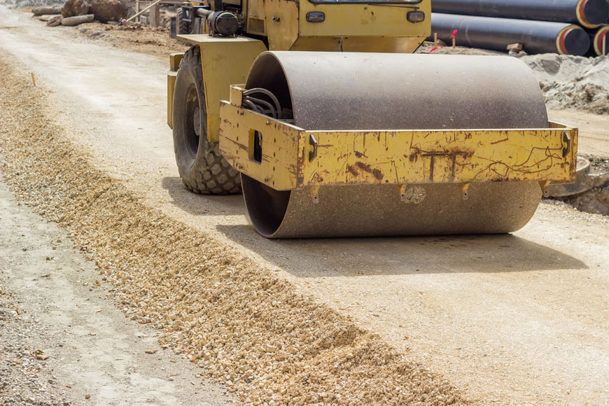 A vibratory steel drum compactor is used to damp down sand as a road base