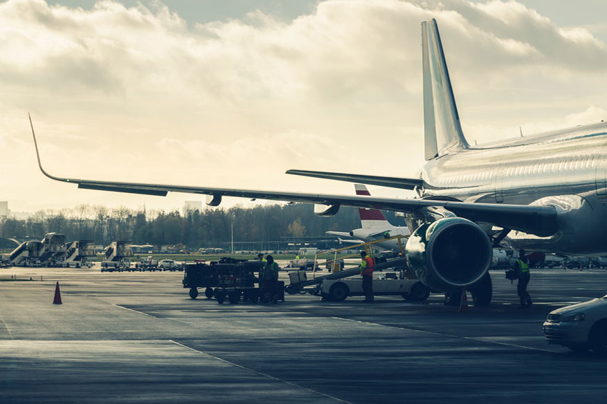 An airplane sits on a tarmac in a small airport on an early morning, a line of trees in the distance.