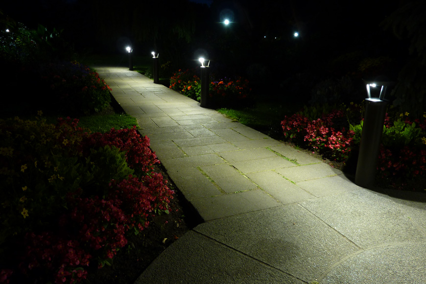 A series of solar lighting bollards illuminates a pathway edged in red flowers