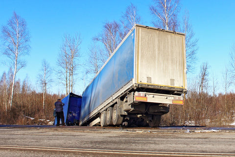 semi-truck stuck in the ditch with the trailer sticking out on the road