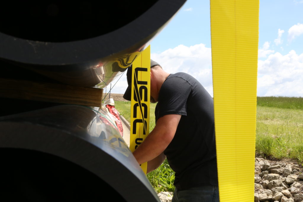 Trucker applying ratchet strap to flatbed trailer