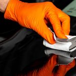 A person's hand applying car wax on black car bonnet